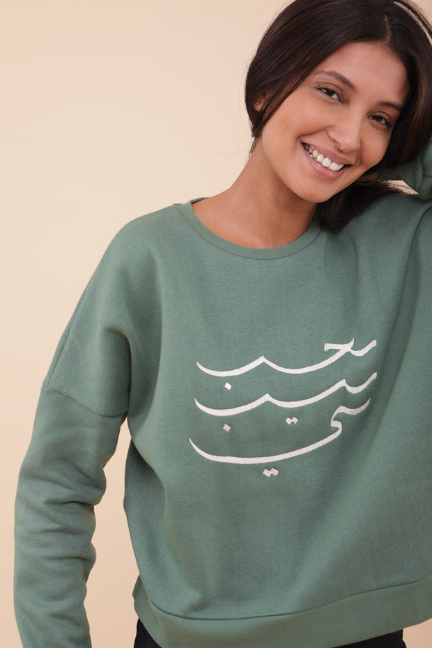 Femme portant le sweat LYOUM avec manches tombantes et calligraphie brodée.