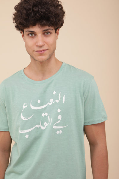 Il porte le t-shirt 'La menthe dans le cœur' en arabe sérigraphiée.