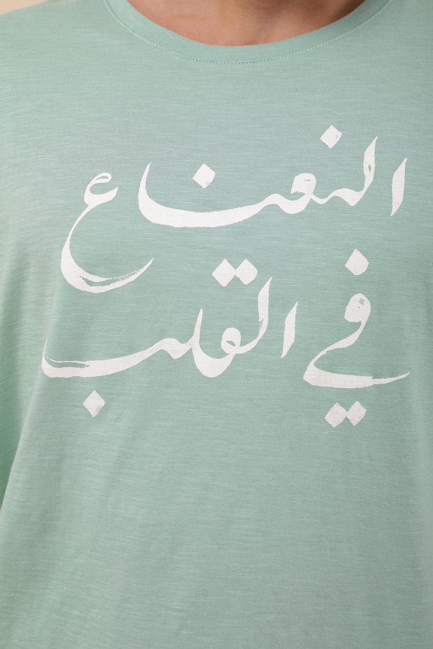 T-shirt vert clair 'La menthe dans le cœur' en arabe sérigraphiée, couleur écru, sur le devant.