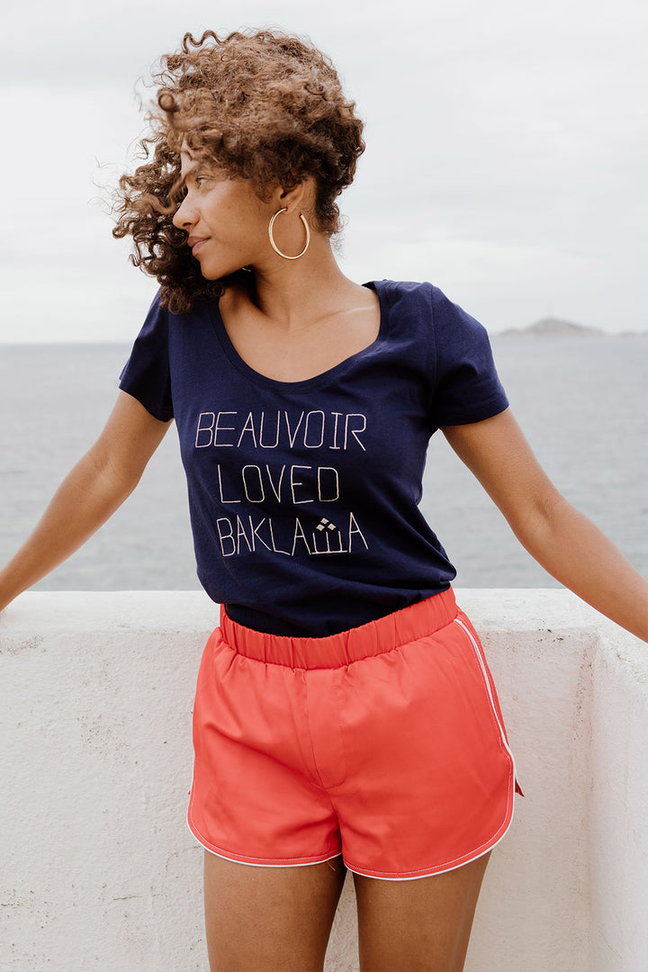 Femme cheveux au vent surplombant la mer en tshirt LYOUM Beauvoir Baklawa.