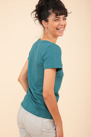 Grand sourire d'une femme brune, en t-shirt LYOUM vert émeraude.