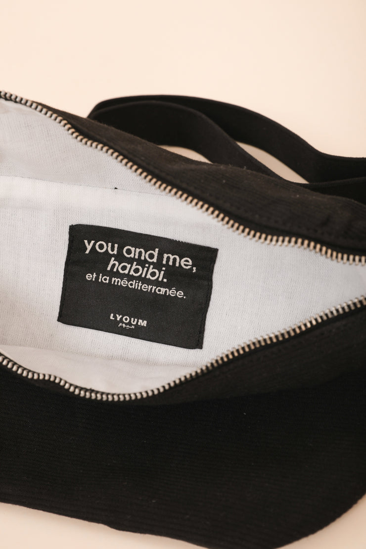Intérieur du sac banane LYOUM noir et son étiquette portant le slogan de la marque.