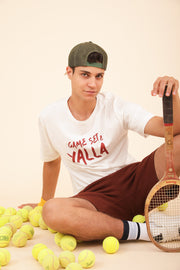 Homme en tshirt LYOUM Sport assis au milieu de balles tennis.