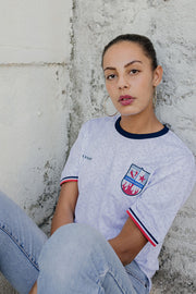 Femme méditerranéenne en maillot LYOUM Harissa United blanc et en jeans.
