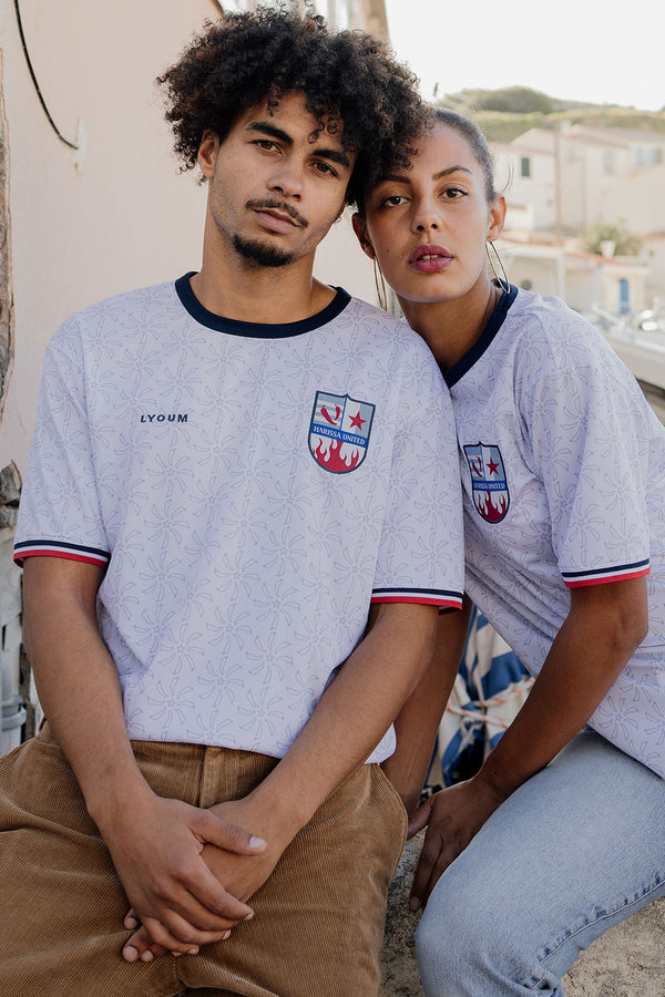 Une femme et un homme assis, portant le maillot LYOUM Harissa United blanc.