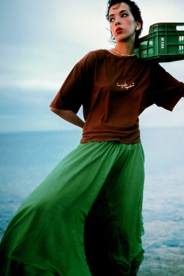 Femme en tshirt LYOUM camel et jupe verte dos à la mer.