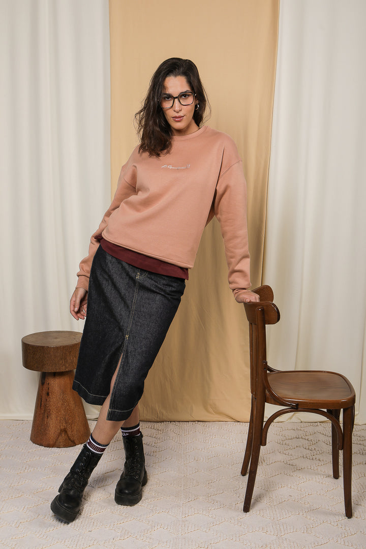 Femme en jupe LYOUM en denim et sweat rose debout appuyée sur une chaise.