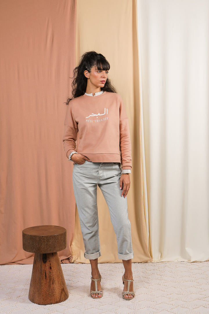 Femme debout posant avec un look complet, portant le sweat méditerranée signé LYOUM.