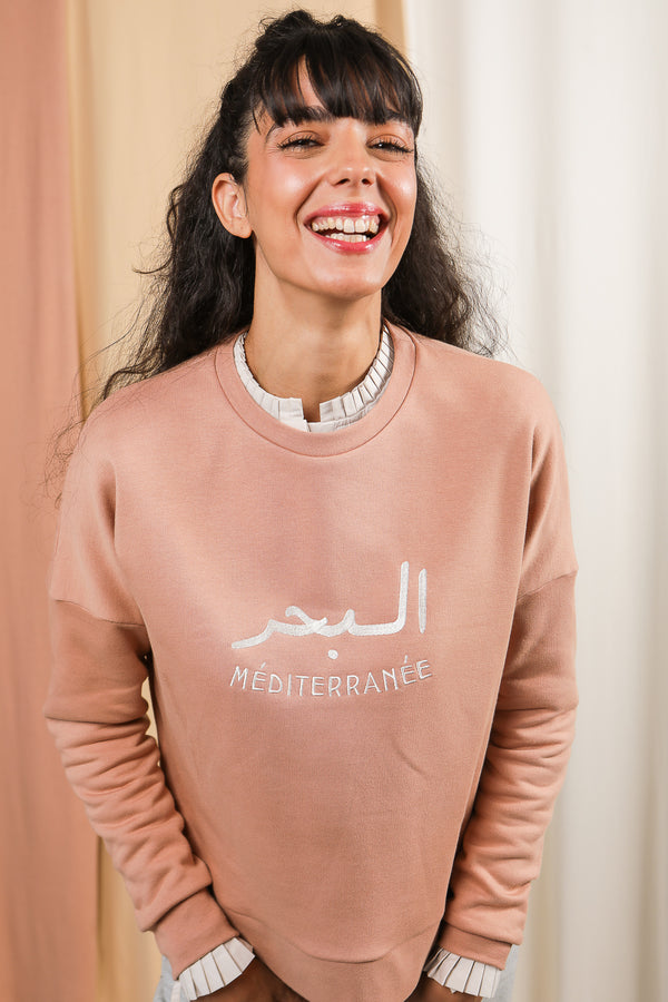 Femme souriante portant le sweat méditerranée en rose signé LYOUM.