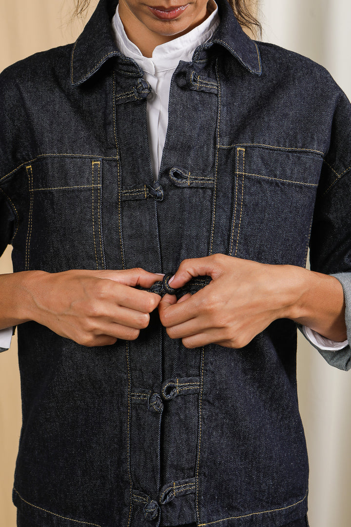 Mains d'une femme qui ferme un bouton de sa veste LYOUM en Denim.