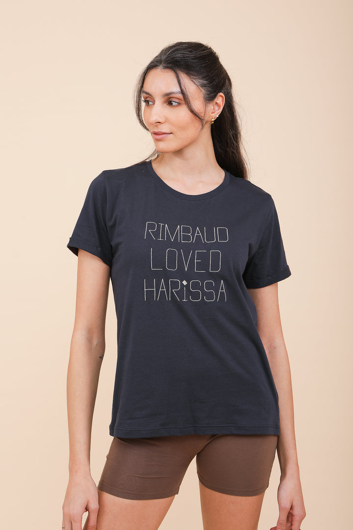 Femme brune en shorty marron et tshirt LYOUM bleu avec mots Rimbaud Loved Harissa.