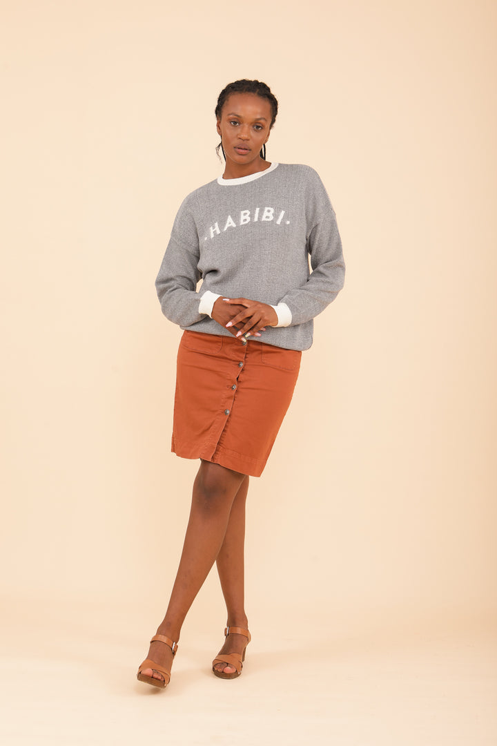 Femme en tenue pull Habibi LYOUM et jupe genou terracotta.