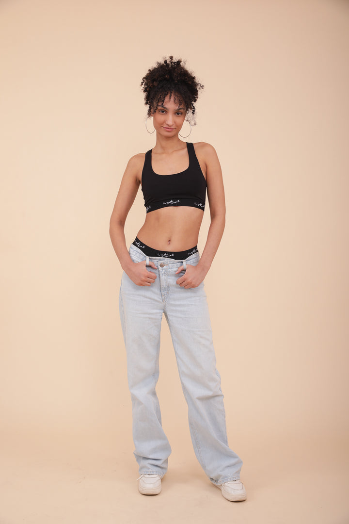 Femme en brassière LYOUM noire et jeans bleu ciel laissant apparaitre la culotte assortie.