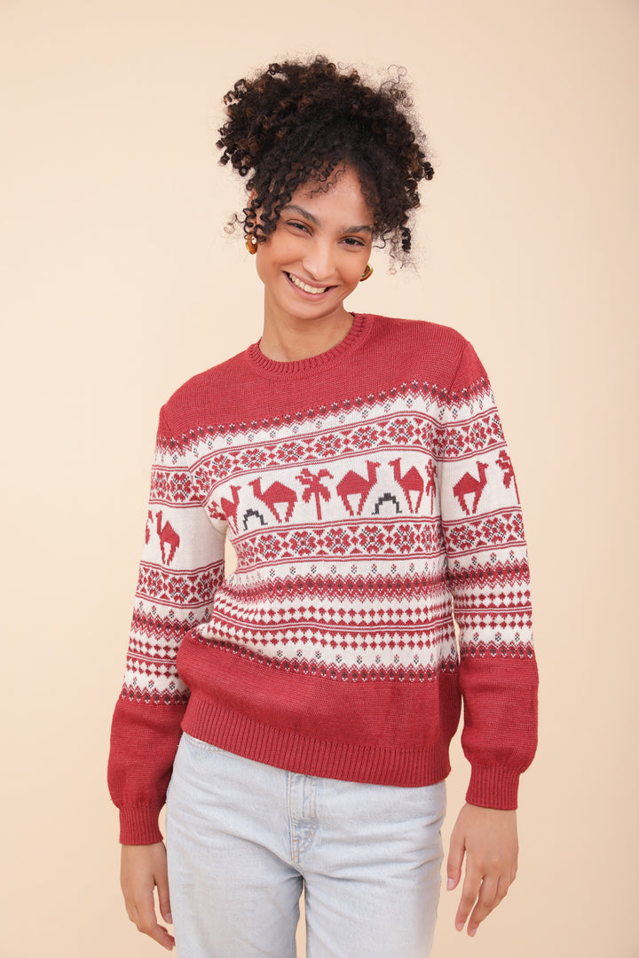 Femme souriante en pull de Noël LYOUM rouge motif dromadaires et palmiers.