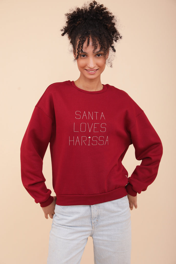 Femme aux cheveux bouclés, portant le sweat LYOUM Santa Loves Harissa.