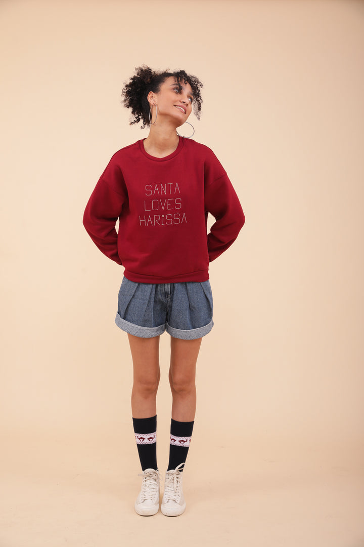 Femme en sweat LYOUM Santa Harissa, short en jeans et chaussettes de Noël.