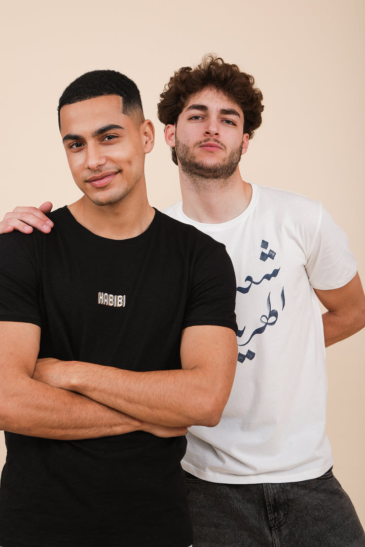 Homme en tshirt LYOUM noir avec homme en tshirt blanc avec calligraphie arabe.