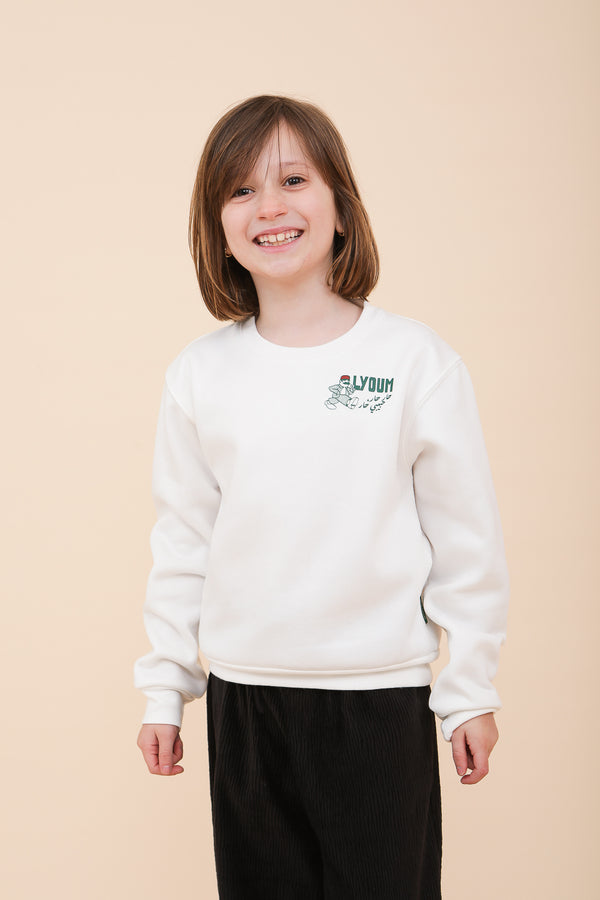 Enfant souriante portant un sweat blanc LYOUM avec logo et inscription 'har har habibi har' en arabe sérigraphiés.