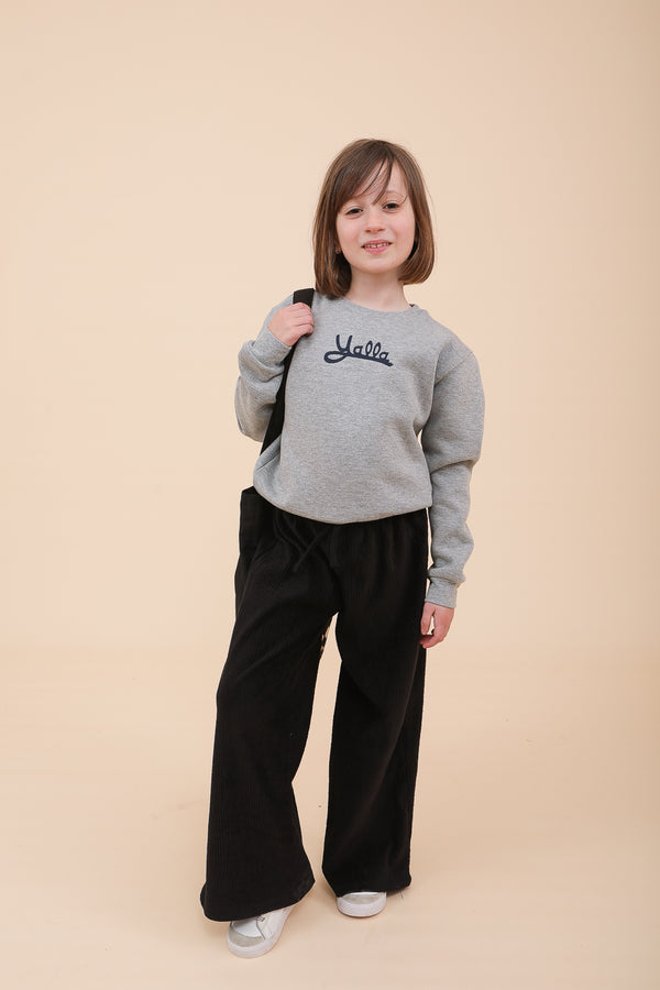 Petite fille posant en portant un sweat LYOUM gris avec la sérigraphie 'Yalla'.