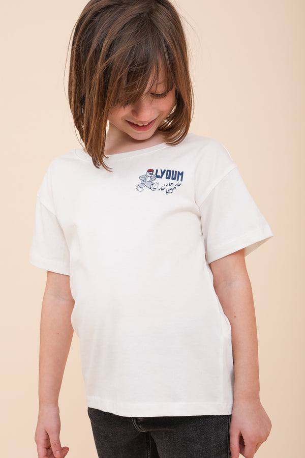 Enfant souriante portant un t-shirt blanc LYOUM en coton, regardant le logo sérigraphié "Har Har Habibi Har" en arabe.