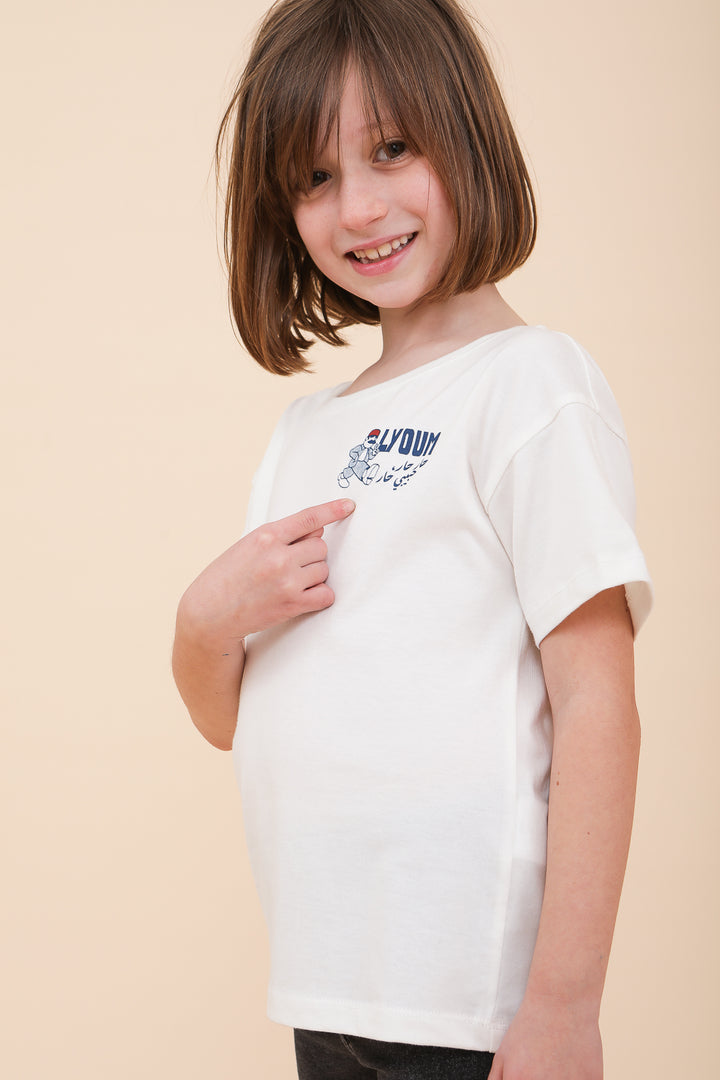Enfant en t-shirt blanc LYOUM, montrant du doigt le motif graphique et calligraphié en arabe.
