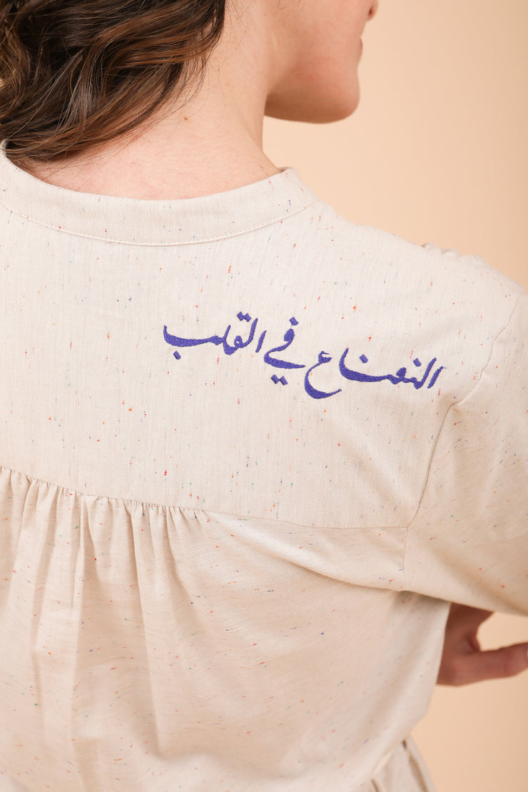 Calligraphie arabe 'La menthe dans le cœur' brodée sur l'épaule en fil bleu.