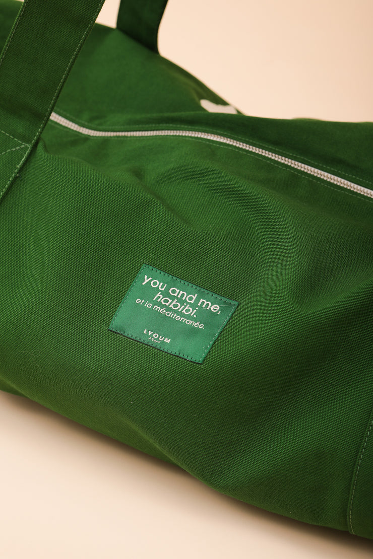 Le sac méditerranéen iconique, de couleur vert sport avec poche intérieure pratique pour ranger facilement vos affaires personnelles et étiquette 'You and Me, Habibi. Et la Méditerranée' cousue sur le devant ton sur ton sur un côté.