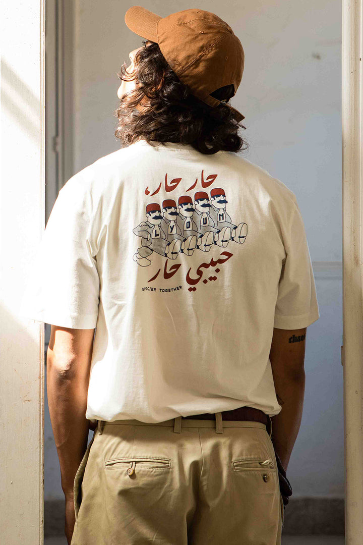 Homme de dos en casquette et tshirt LYOUM à illustration personnages baba qui marchent.