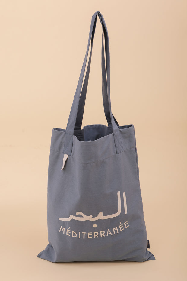 Tote Bag en toile, avec poche et anses intérieures, couleur bleu clair. Broderie 'La Mer Méditerranée' en mix arabe et français sur un côté, en fil écru.