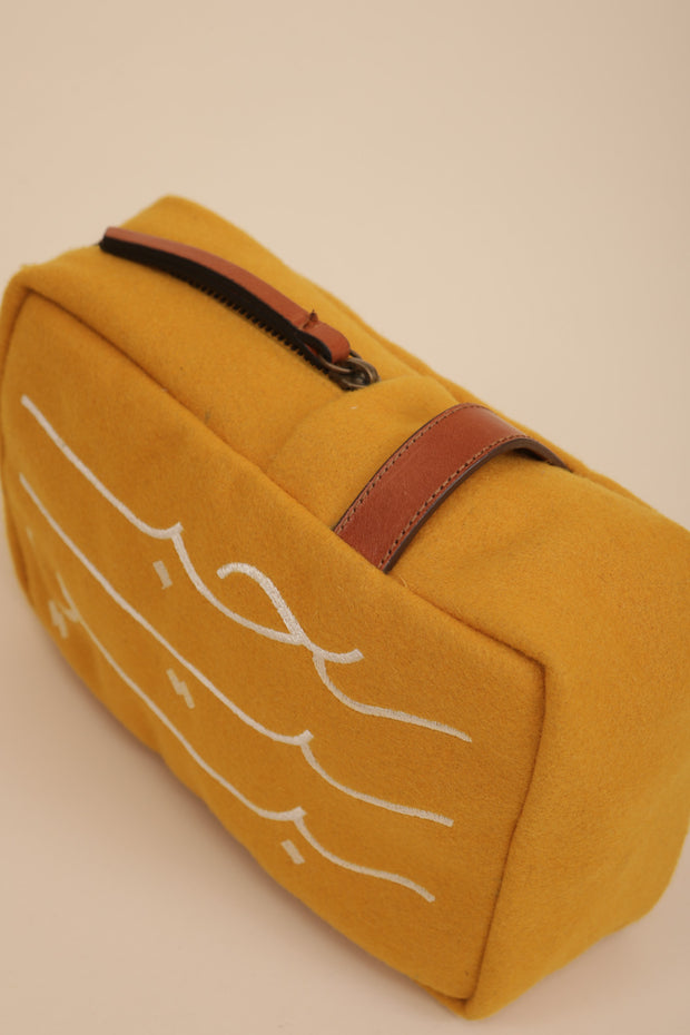 Pochette en drap de laine doublé, couleur jaune, avec anse en cuire camel. Calligraphie 'Habibi' ('Mon Amour' en arabe) brodée sur le devant.