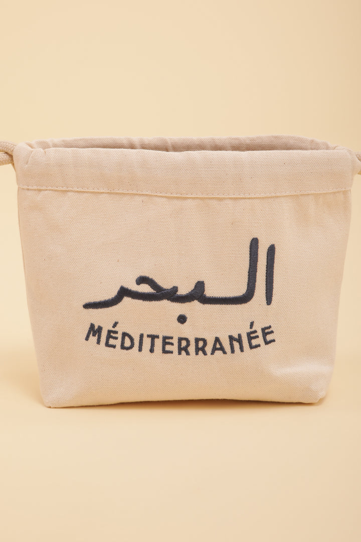 Découvrez notre modèle iconique dans notre ligne de pochette, Pouch Méditerranée, notre message exclusif 'La Mer méditerranée' en arabe/français brodé sur un côté, en fil bleu navy.