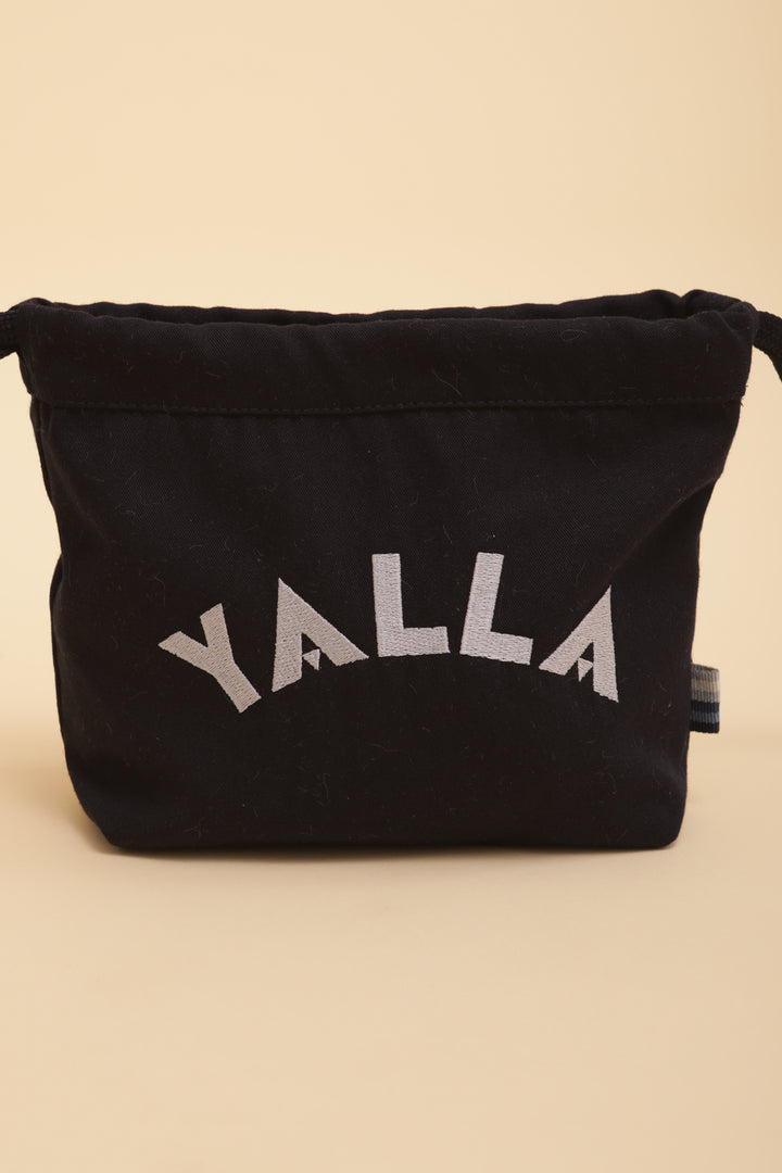 Découvrez la petite pochette à coulisse, doublée, avec 'Yalla' brodé sur le devant.