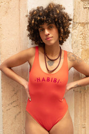 Maillot une-pièce pour femmes by LYOUM. Le maillot Habibi corail et intemporel pour vos journées plages avec l'iconique 'Habibi' ('Mon amour' en arabe) sur le devant.