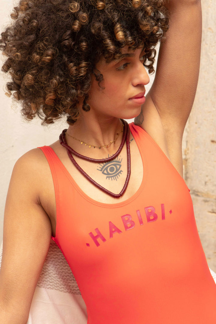 Maillot une-piece pour femmes by LYOUM. Le maillot Habibi corail et intemporel pour vos journées plages avec l'iconique 'Habibi' ('Mon amour' en arabe) sur le devant