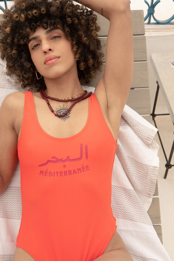  Maillot une-pièce pour femmes by LYOUM. Le maillot Mer Méditerranée corail et intemporel pour vos journées plages avec l'iconique 'La Mer Méditerranée' by LYOUM en arabe/français sur le devant.