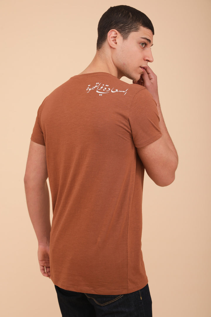 Nouveau t-shirt LYOUM pour homme. Coupe droite indémodable et col V élégant, le tout dans une matière douce et fluide en coton, couleur marron sable. Message exclusif 'Le Bonheur est dans le Café', en calligraphie arabe derrière l'épaule.