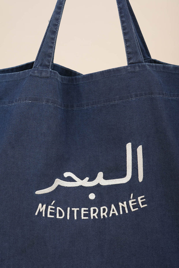 Grand sac de plage en toile de coton bleu moyen avec broderie 'La Mer Méditerranée' en arabe et français, couleur crème.