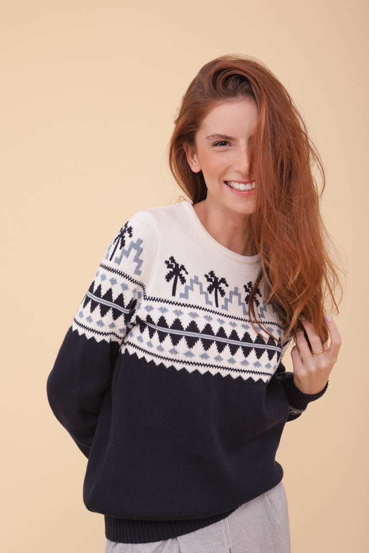 Femme rousse en pull de Noël LYOUM bleu motif palmiers.