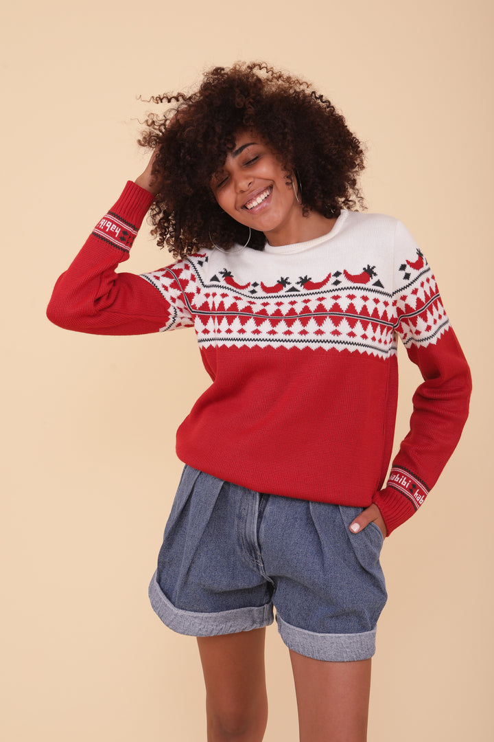 Femme aux cheveux bouclés en pull de Noël LYOUM rouge et short en jeans.